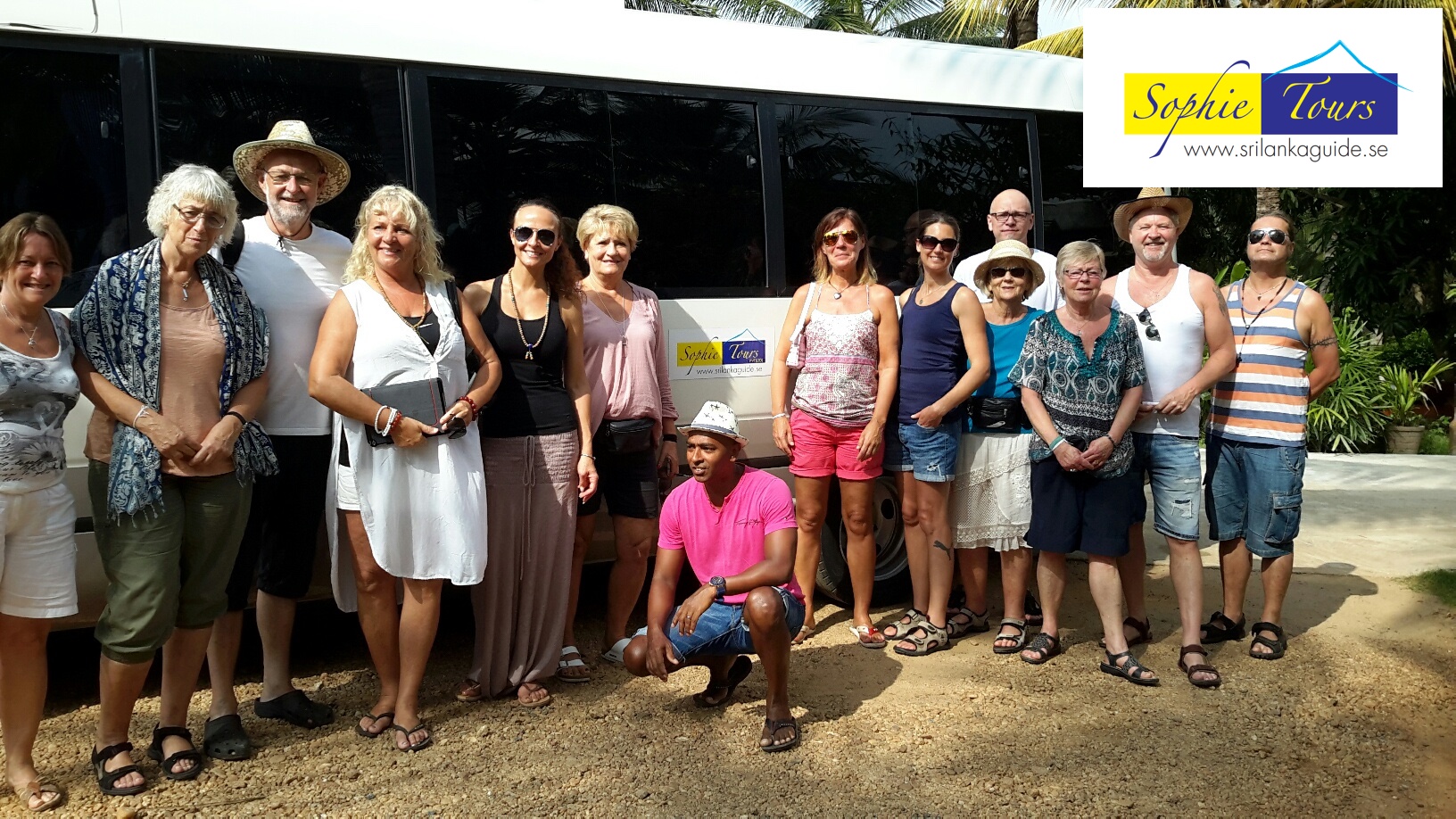 An image of summery dressed tourists, in front of a white bus, with the Sophie Tours logo on it. Jungle looms in the background.