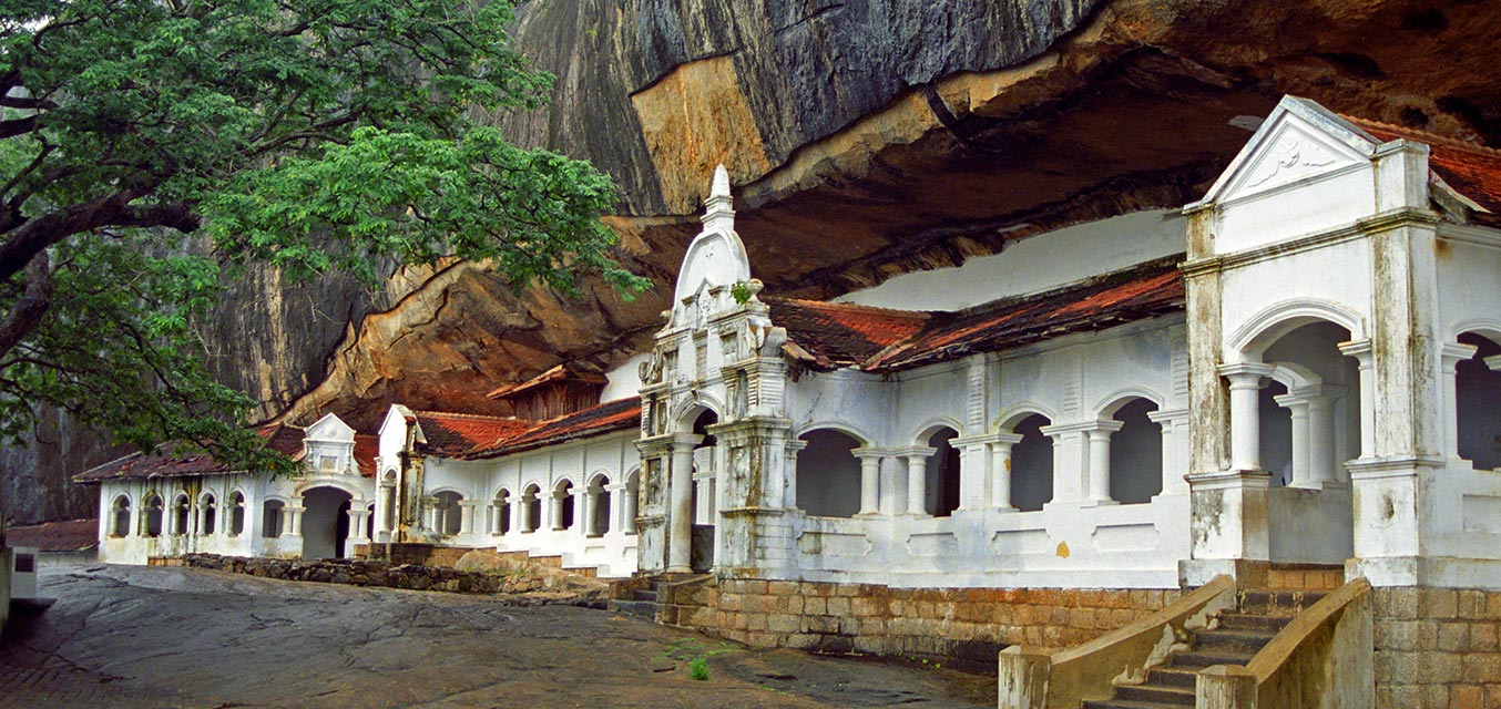 A picture of Dambulla cave temple, a white building in a large cave opening.