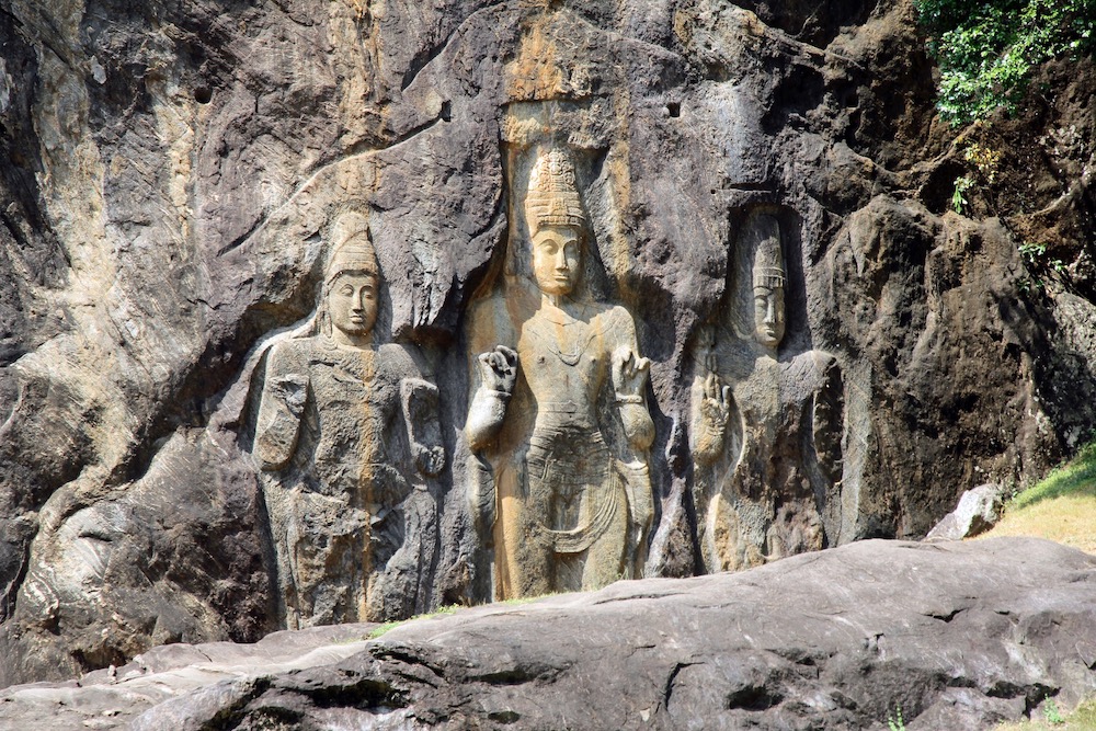 A picture of rock carvings in Buduruwagala, Sri Lanka. Three human figures on the side of a cliff.