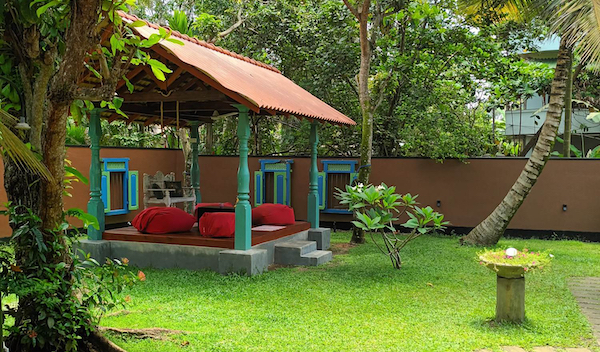 A picture of a garden with a gazebo. In the background a wall and trees.