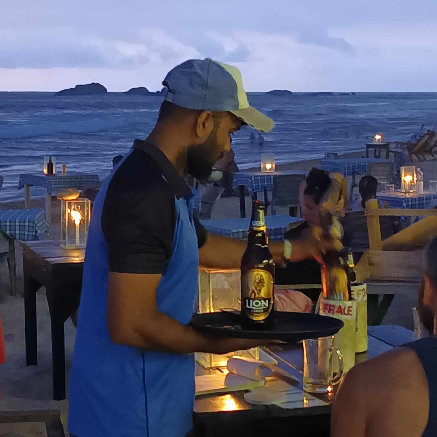 A close-up picture of a person serving beer in a beach bar at dusk. The sea in the background.