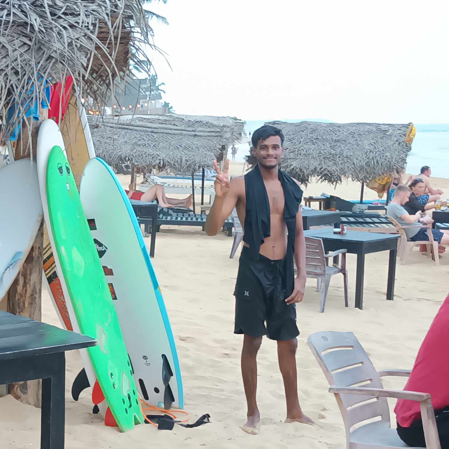 A picture of surfboards lined up on the beach and a young man in swimming trunks.